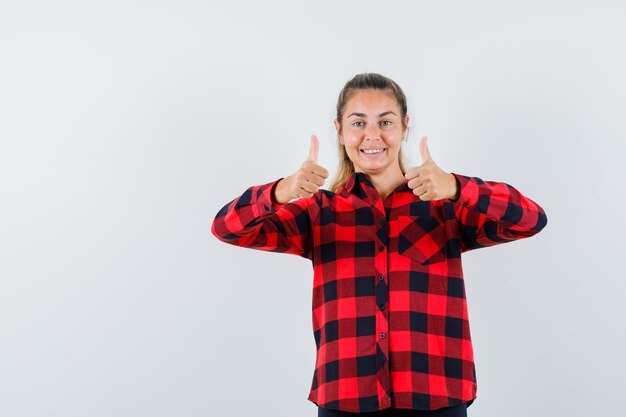 Young lady in casual shirt showing double thumbs up and looking glad , front view.