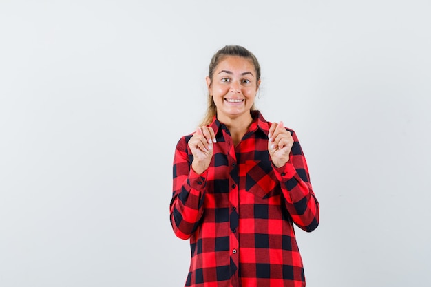 Young lady in casual shirt showing fig gesture and looking cheerful , front view.