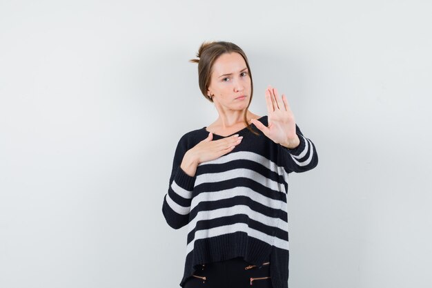 Young lady in casual shirt showing stop gesture and looking serious
