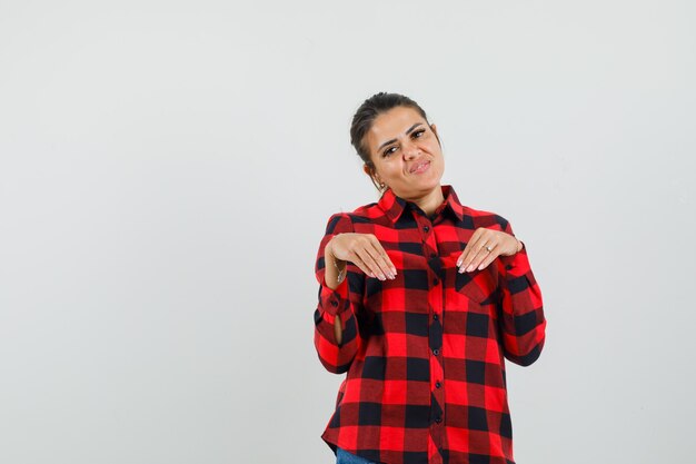 Young lady in checked shirt doing funny gesture with hands and looking amused