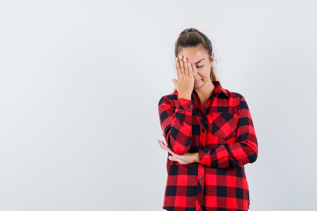 young lady in checked shirt holding hand on face and looking tired