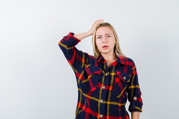 Free photo young lady in checked shirt holding hand on head and looking puzzled , front view.