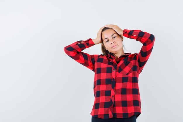 Young lady in checked shirt holding hands on head and looking elegant