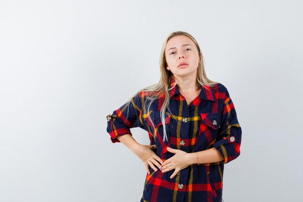 Young lady in checked shirt holding hands on stomach and looking unwell , front view.