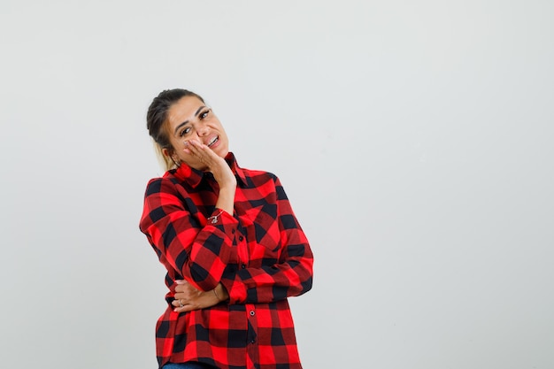 Young lady in checked shirt leaning cheek on raised palm and looking pensive