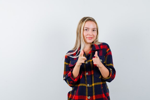 Young lady in checked shirt pointing at camera and looking positive , front view.