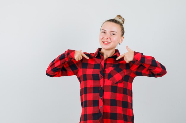 Young lady in checked shirt pointing at herself and looking confident