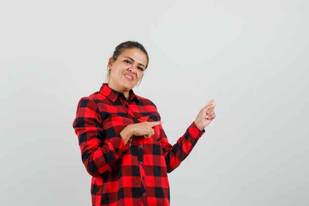 Young lady in checked shirt pointing to the side and looking jolly