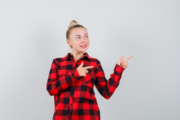 Young lady in checked shirt pointing to the side and looking optimistic