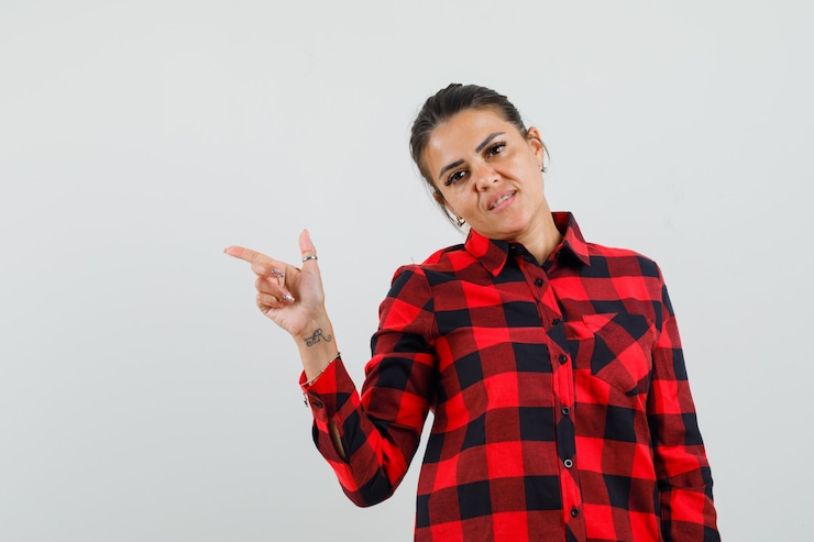 मुफ़्त फोटो young lady in checked shirt pointing to the side and looking sensible