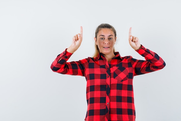 Young lady in checked shirt pointing up and looking confident