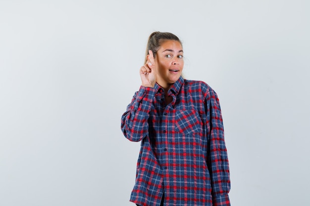 Young lady in checked shirt pointing up and looking intelligent , front view.