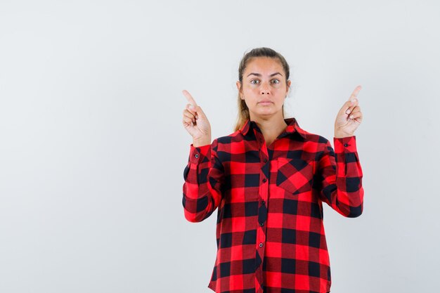 Young lady in checked shirt pointing up and looking puzzled