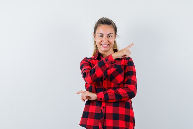 Young lady in checked shirt pointing at upper right corner and looking cheerful