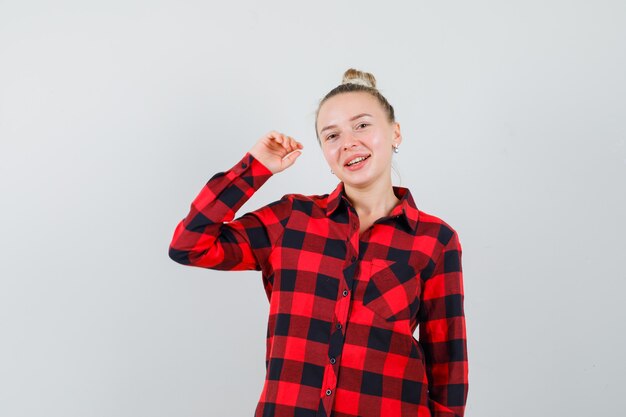 Young lady in checked shirt posing while raising arm and looking merry