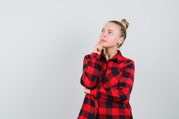 Free photo young lady in checked shirt propping chin on hand and looking pensive