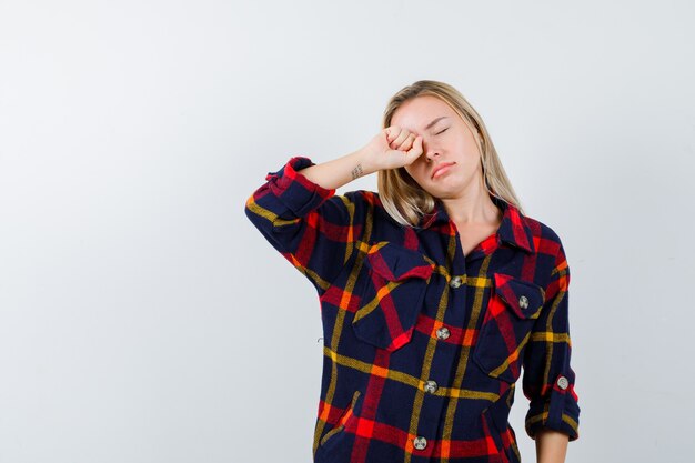 Young lady in checked shirt rubbing eye and looking sleepy , front view.