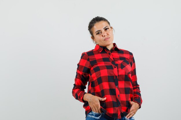 Young lady in checked shirt, shorts holding hands in pockets and looking confident