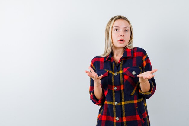 Young lady in checked shirt showing helpless gesture and looking puzzled , front view.