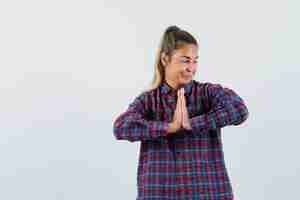 Free photo young lady in checked shirt showing namaste gesture and looking hopeful , front view.