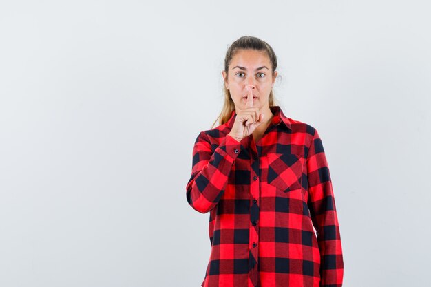 Young lady in checked shirt showing silence gesture and looking careful