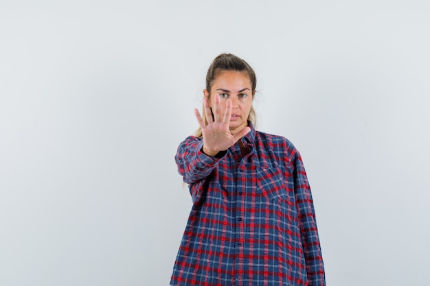 Young lady in checked shirt showing stop gesture and looking confident , front view.