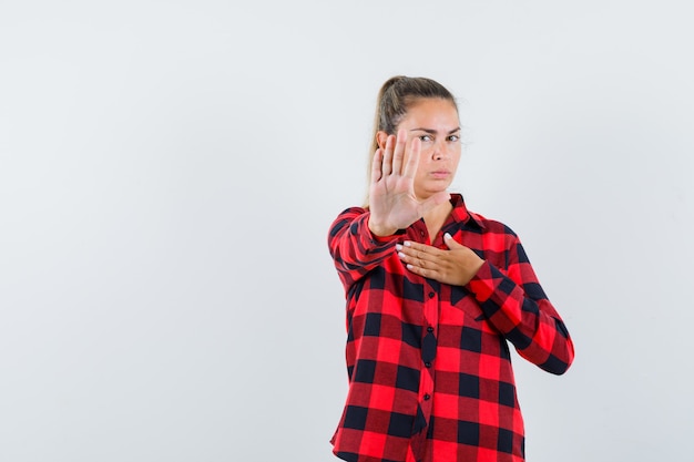 Foto gratuita giovane donna in camicia a quadri che mostra il gesto di arresto e che sembra seria