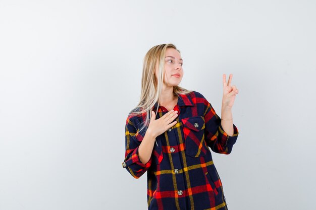 Young lady in checked shirt showing victory sign and looking blissful , front view.