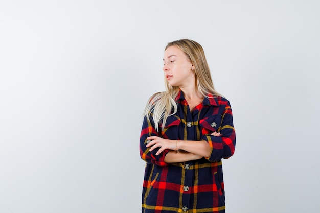 Young lady in checked shirt standing with crossed arms while looking away and looking confident , front view.