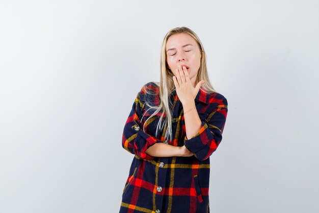 Young lady in checked shirt yawning and looking sleepy , front view.