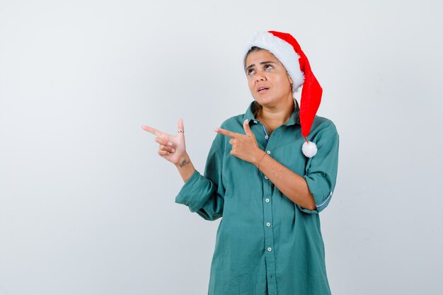 クリスマスの帽子をかぶったお嬢様、シャツは左側を指して不安そうな正面図。