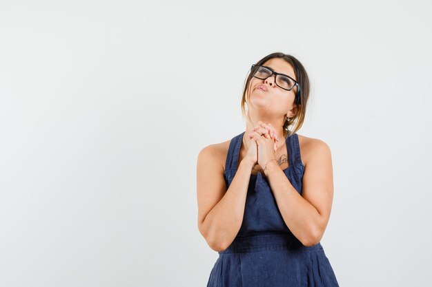 Young lady clasping hands in praying gesture in dress and looking hopeful