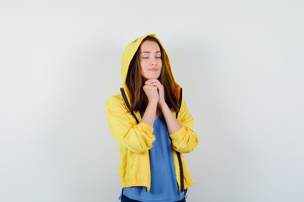 Young lady clasping hands in praying gesture in t-shirt, jacket and looking hopeful. front view.