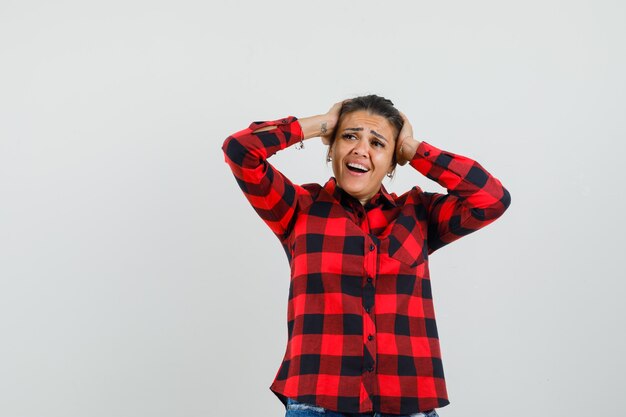 Young lady clasping head in hands in checked shirt and looking excited. 