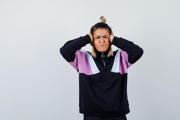 Young lady clasping head with hands in hoodie sweater and looking annoyed