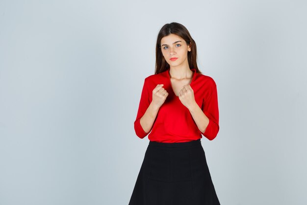 Free photo young lady clenching fists in red blouse, black skirt and looking confident