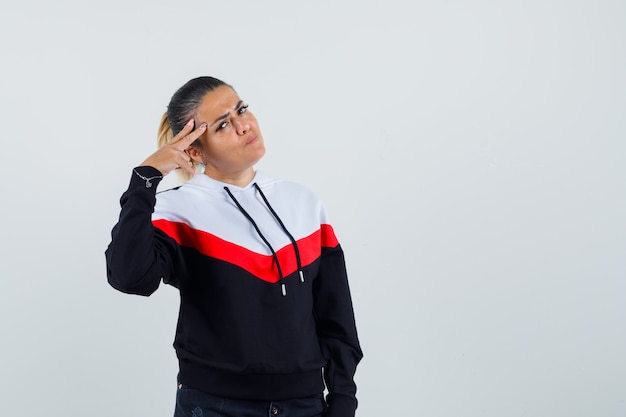 Young lady in colorful sweatshirt holding fingers on her forehead , front view. 