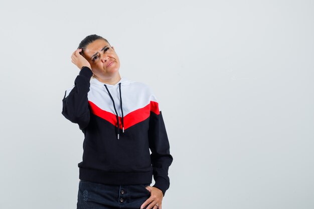 Young lady in colorful sweatshirt looking up while thinking and looking uncomfortable , front view.