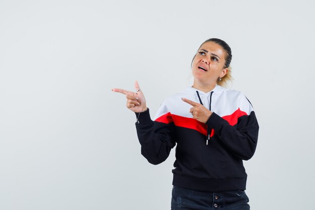 Young lady in colorful sweatshirt pointing aside and looking focused , front view.