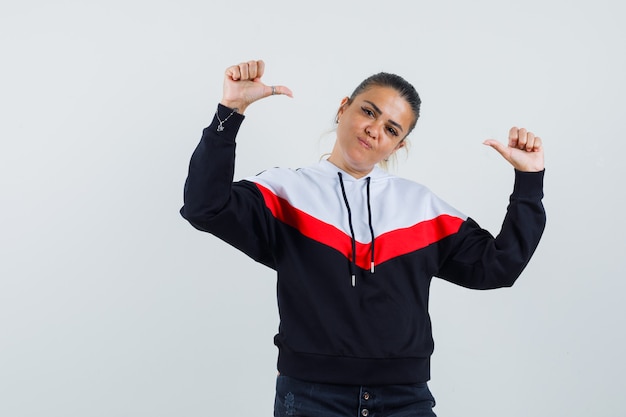 Young lady in colorful sweatshirt showing thumb up and looking self-confident , front view.