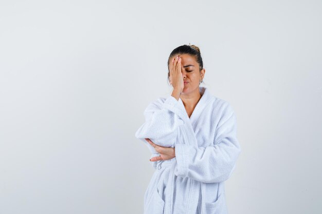 Young lady covering eye with hand in bathrobe and looking confident