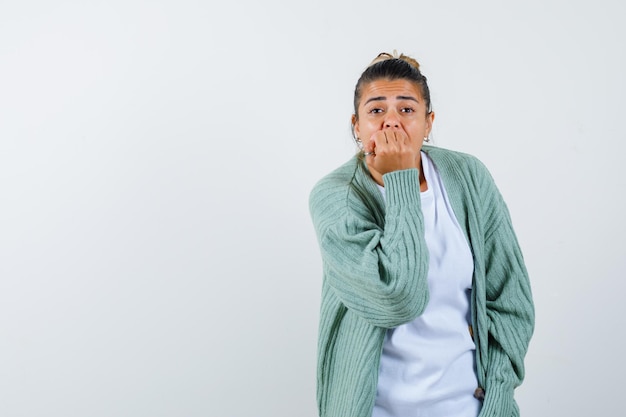 Young lady covering mouth with fist in t-shirt, jacket and looking thoughtful