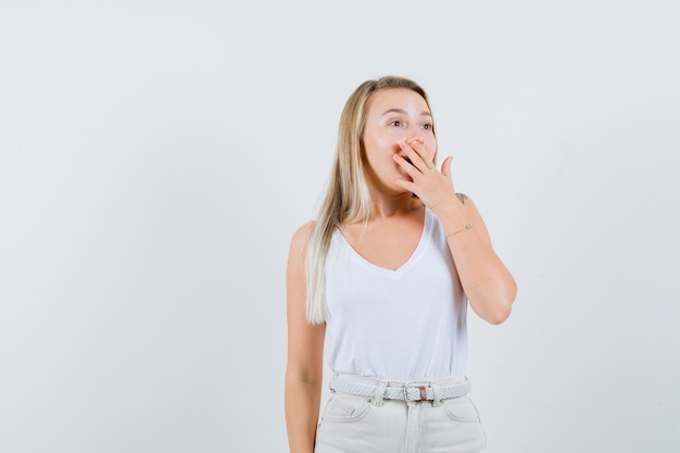 Young lady covering mouth with hand in white blouse and looking astonished