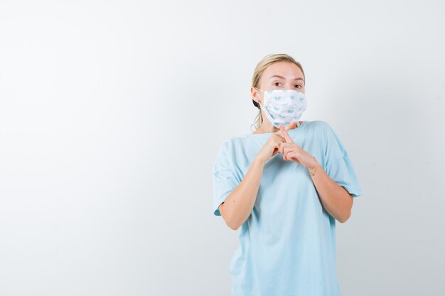 Young lady crossing fingers forming an x in t-shirt, mask and looking confident isolated