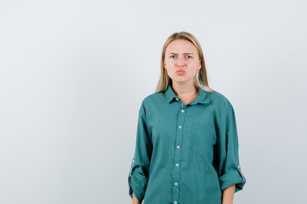 Foto gratuita giovane donna che curva le labbra in camicia verde e sembra cupa