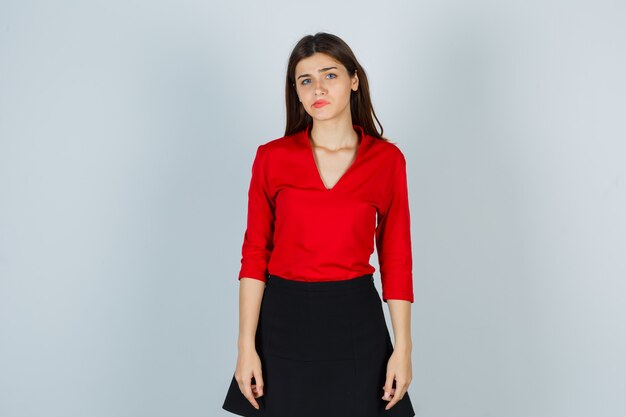 Young lady curving lips in red blouse, black skirt and looking disappointed