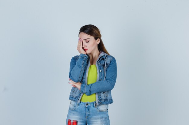 Young lady in denim outfit suffering from migraine and looking fatigued , front view.