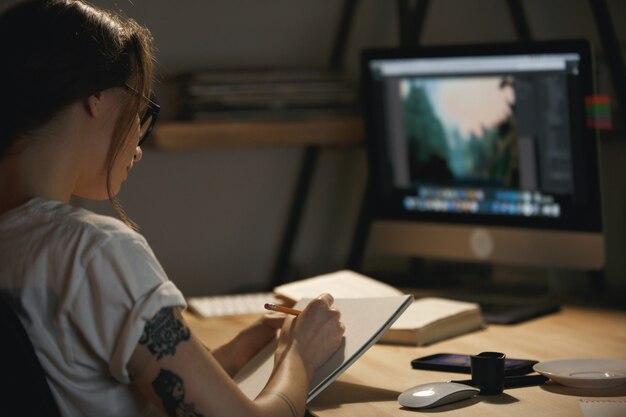 Young lady designer sitting indoors at night drawing sketches