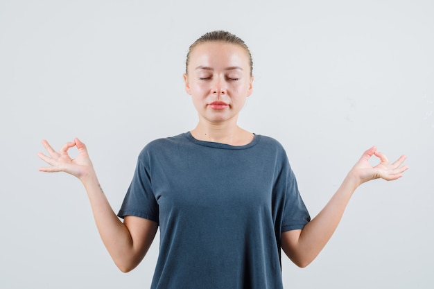 Young lady doing meditation in grey t-shirt and looking peaceful