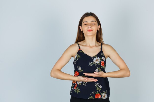 Young lady doing meditation with shut eyes in blouse and looking peaceful. front view.